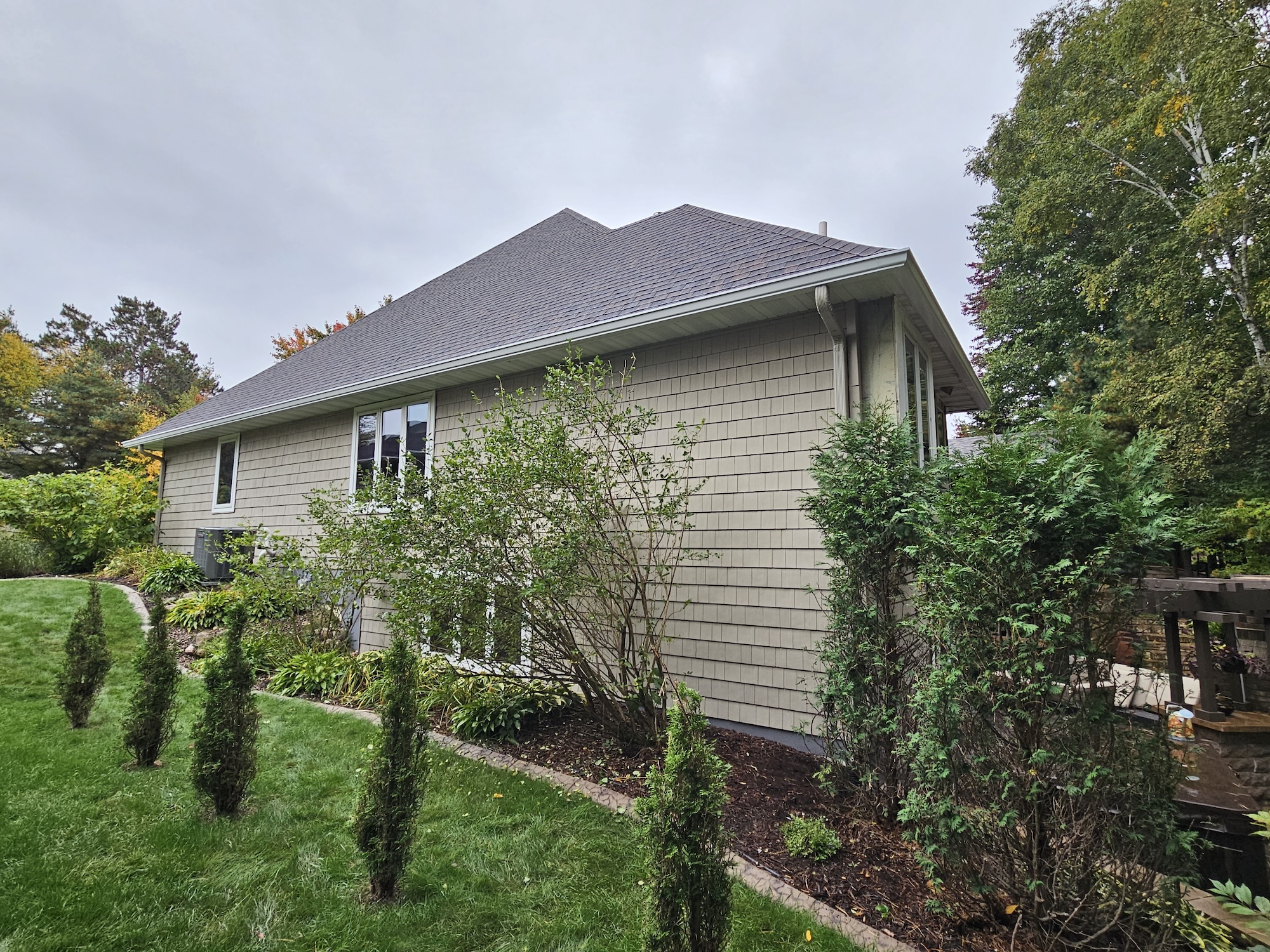 Side view of a Wisconsin home with a brown architectural shingle roof, white trim, and landscaped yard.