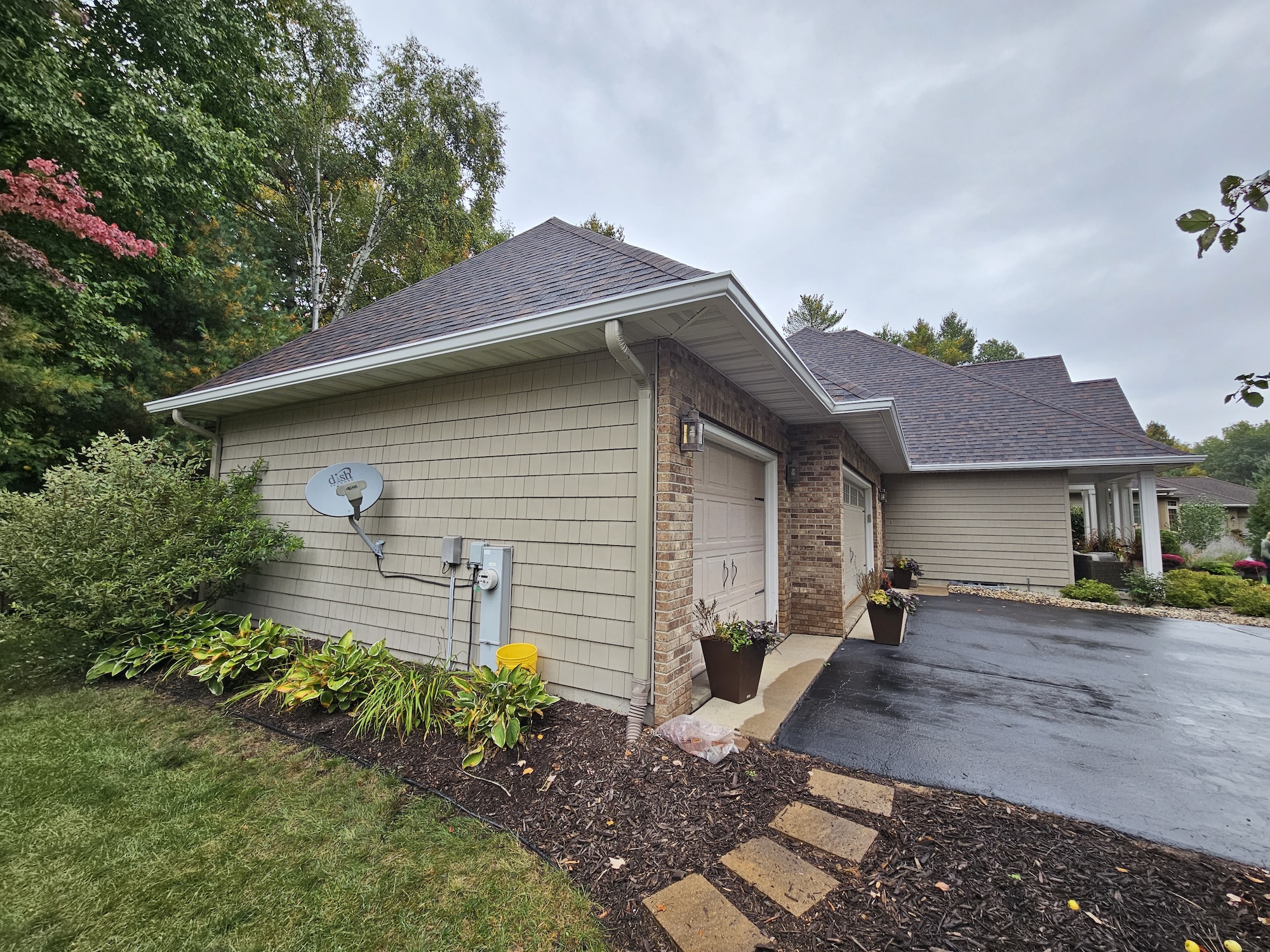 Side garage view of a Wisconsin home with a brown architectural shingle roof, brick accents, and neutral siding.