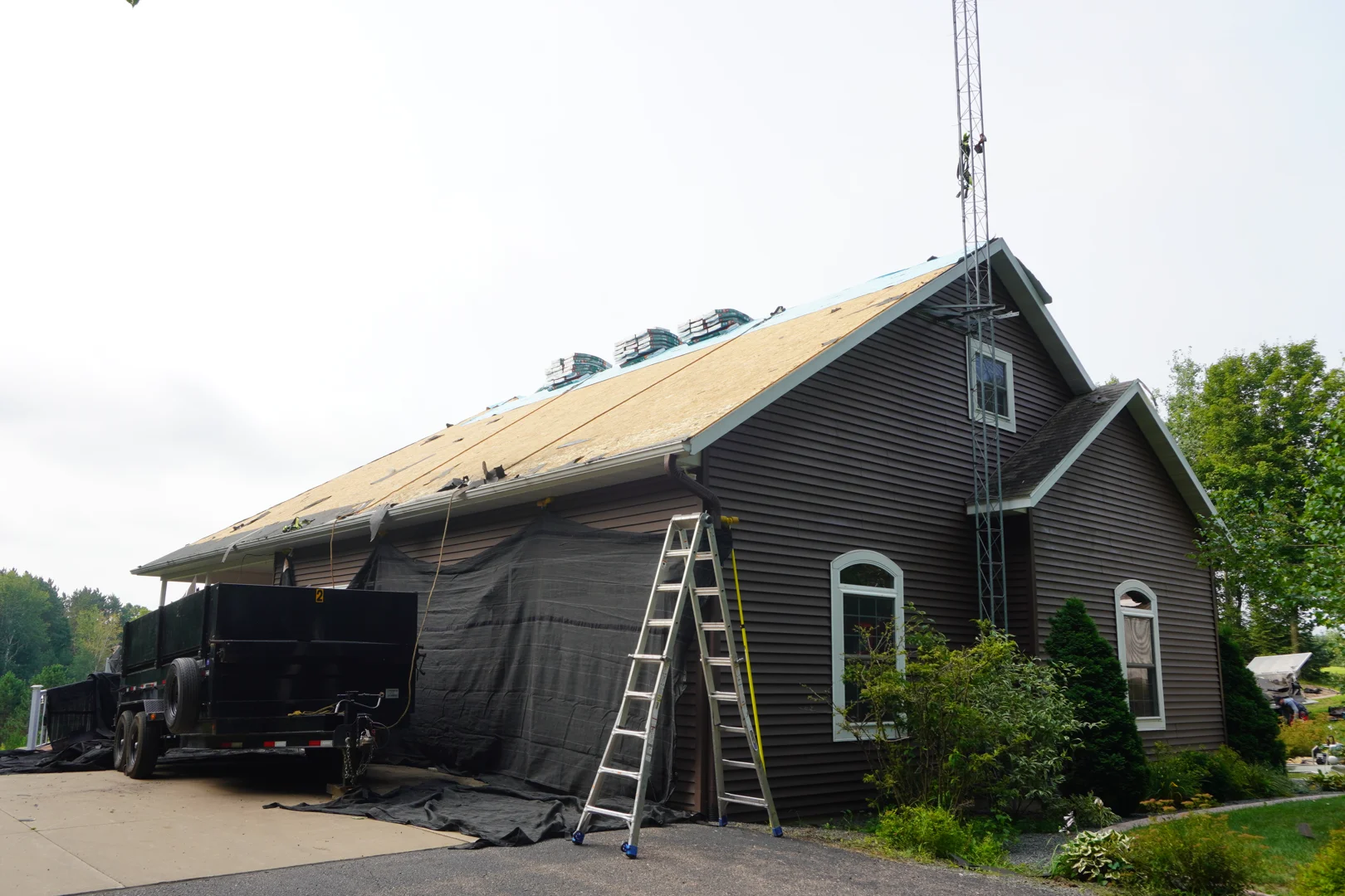 Roof decking exposed during a tear-off on a Central Wisconsin home, with tarps and a dump trailer on site Roof decking exposed during a tear-off on a Central Wisconsin home, with tarps and a dump trailer on site
