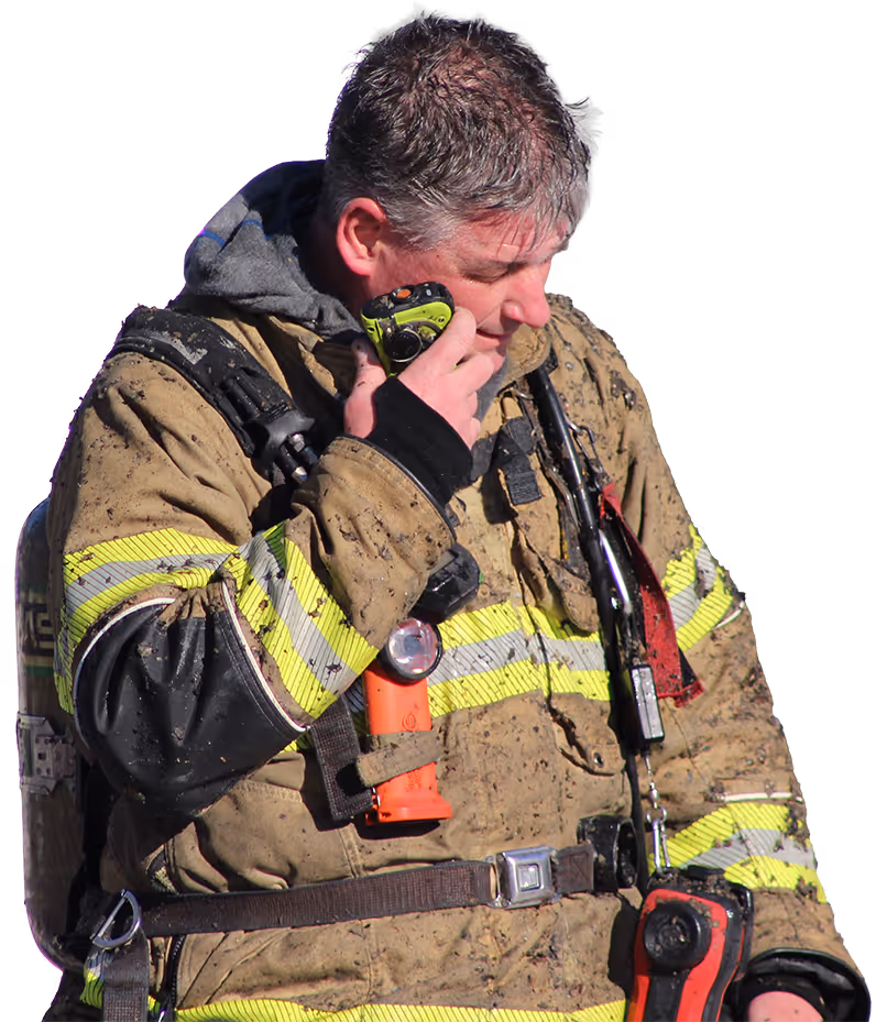 Firefighter wearing full gear and helmet carrying a coiled fire hose over one shoulder and holding a fire axe.