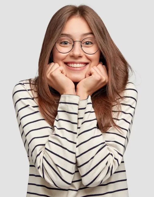 Smiling young woman with glasses wearing a white and black striped long-sleeve shirt, resting her chin on her fists.
