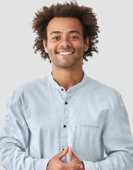 Smiling young man with curly hair wearing a light blue buttoned shirt against a plain background.