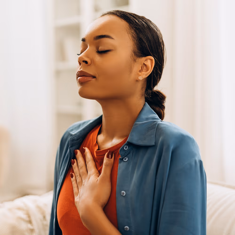 Woman with eyes closed and hand on chest practicing mindfulness or meditation indoors.