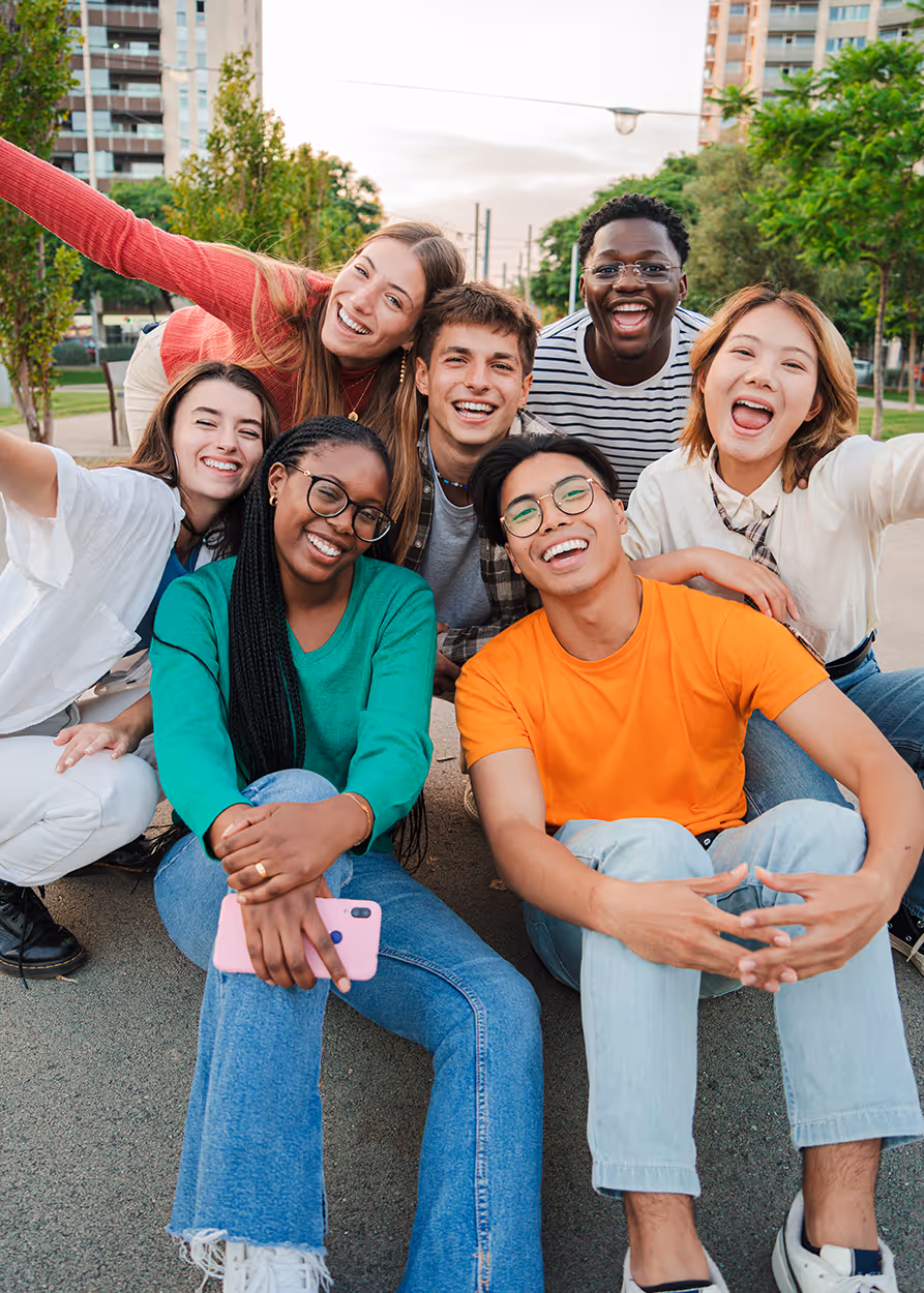 Group of seven diverse young adults sitting and smiling together outdoors in a park.