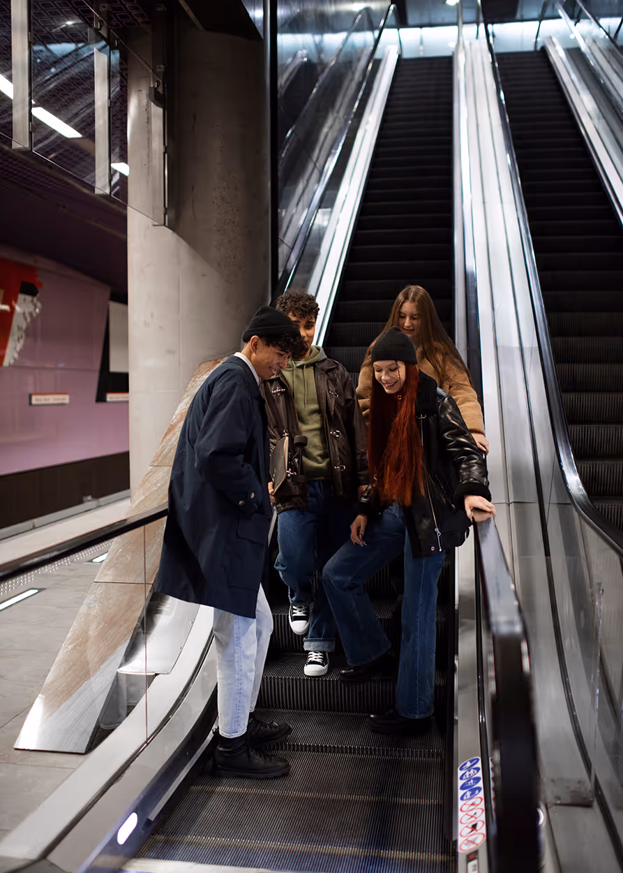 Four young adults standing together and smiling on a descending escalator in an indoor modern space.