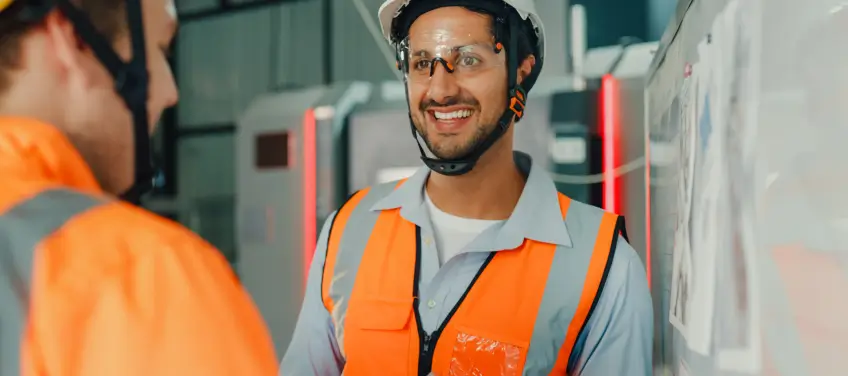 Two construction workers in safety vests and helmets discussing plans on a site.