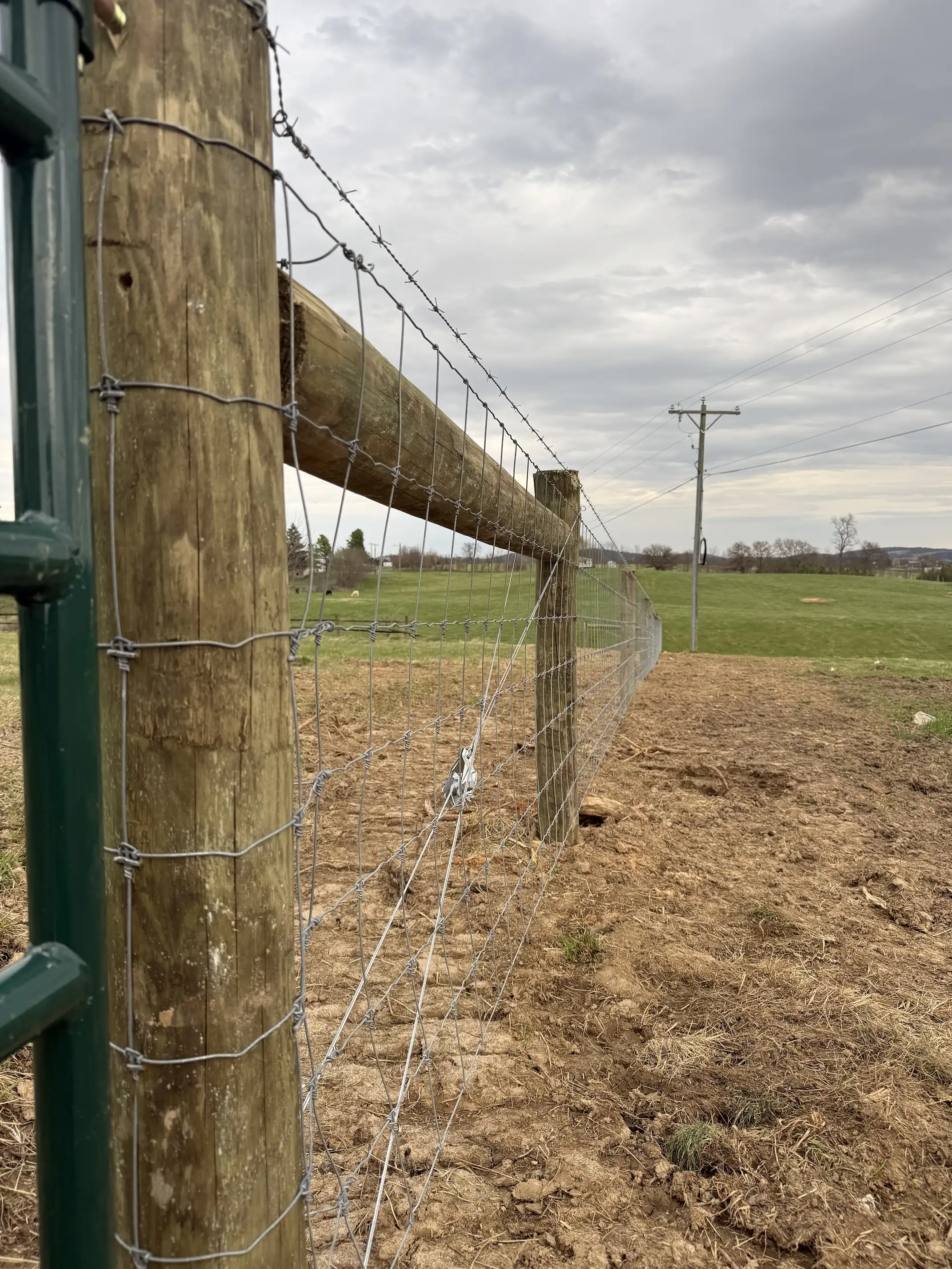 Wooden post and wire fence stretching across a field under a cloudy sky.