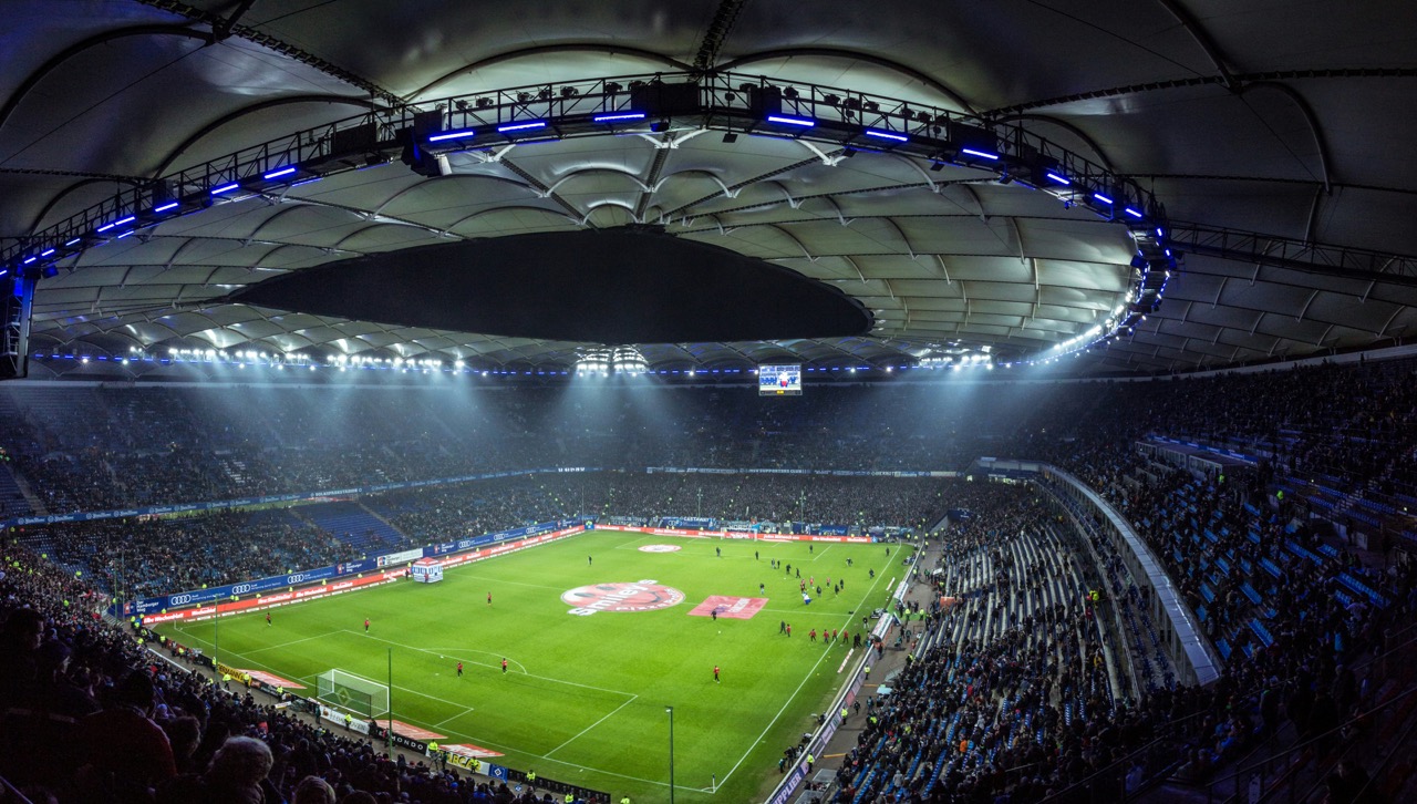 Wide view of a brightly lit soccer stadium at night with a green field and spectators filling most seats.