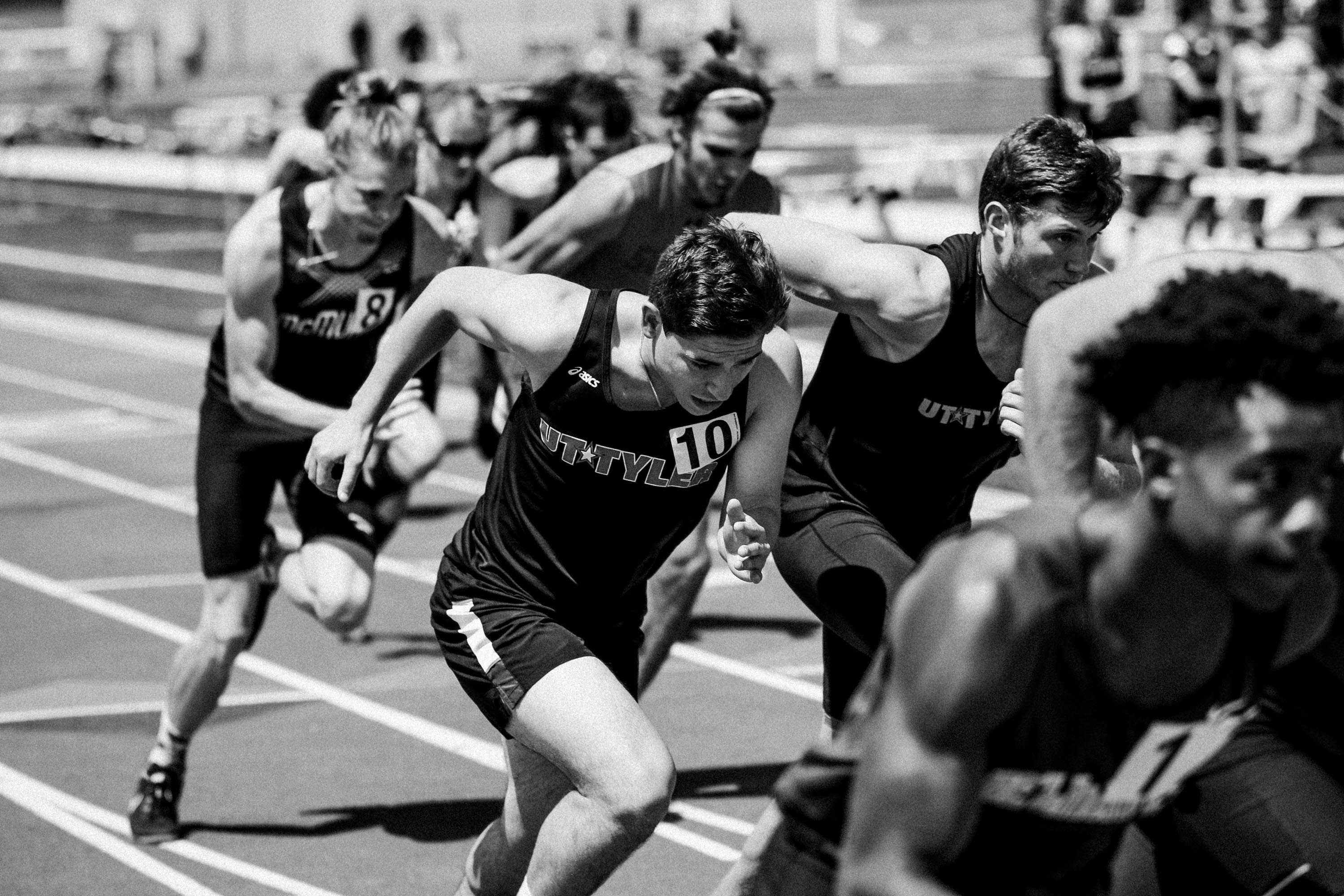 Male athletes in athletic gear sprinting on an outdoor track during a race.