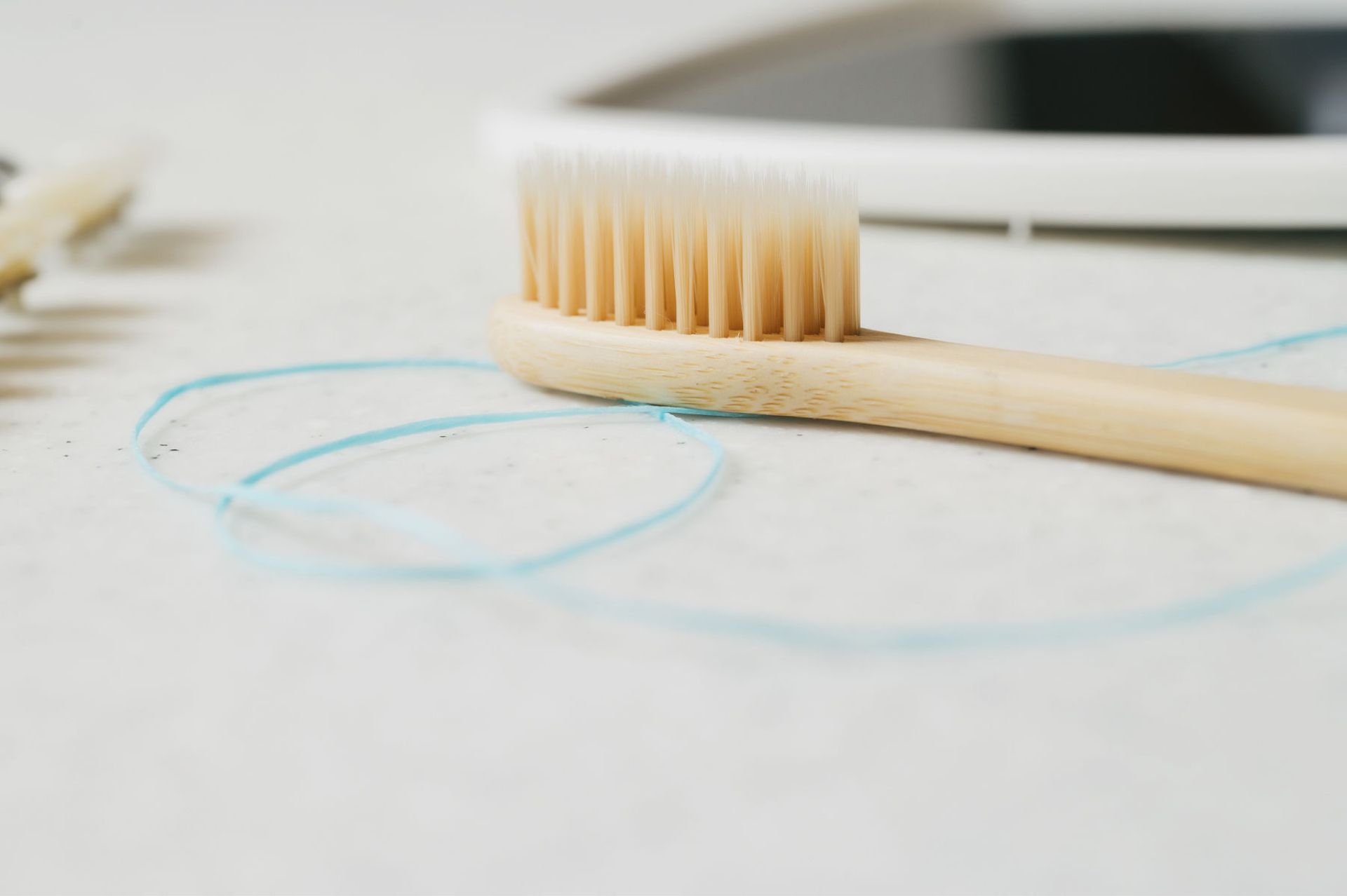 Bamboo toothbrush and a loop of blue dental floss on a white surface.