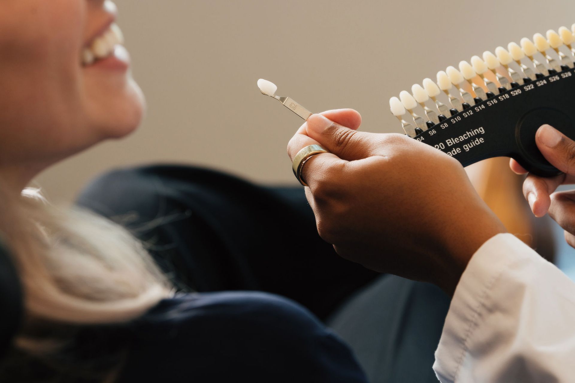 A person holds a dental shade guide near a smiling woman's teeth for color matching.