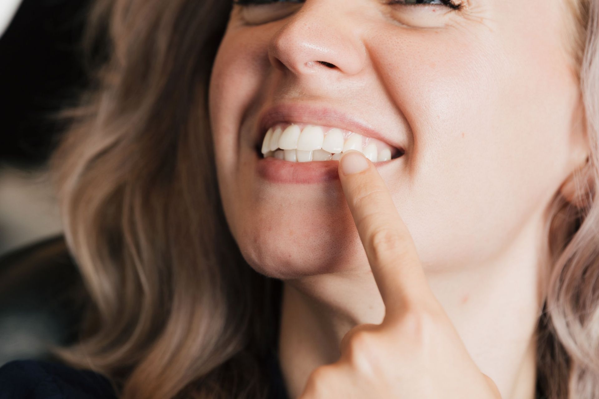 Woman smiling and pointing to her white teeth with her finger.