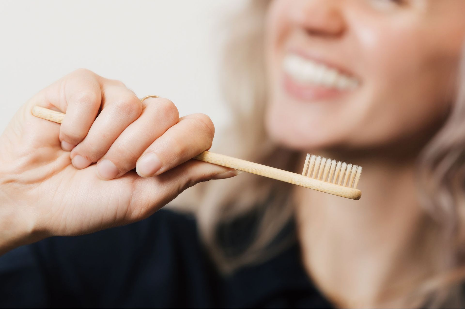 Person holding a bamboo toothbrush with a smile in the blurry background.