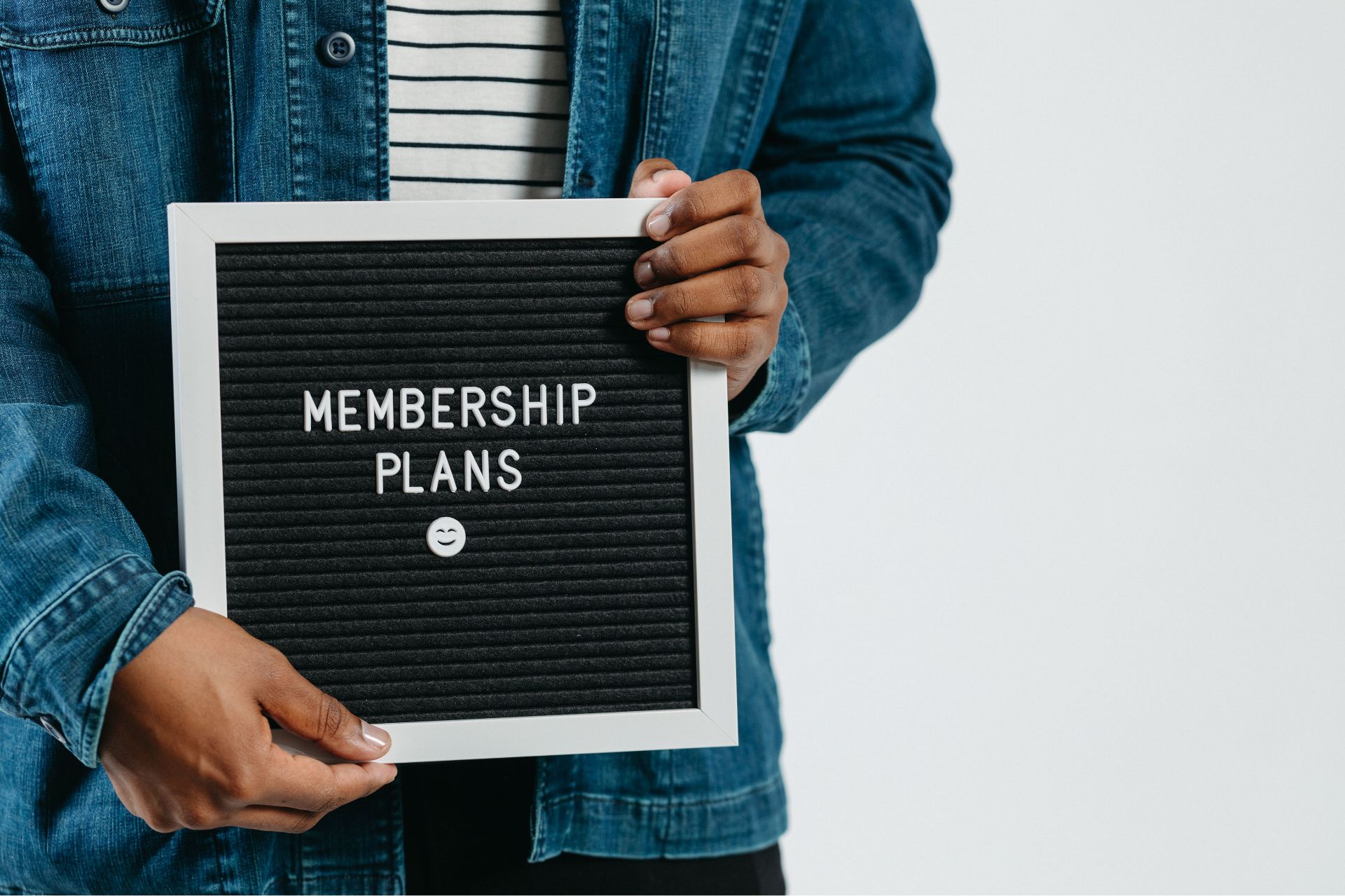 Person holding a black letterboard sign that reads 'MEMBERSHIP PLANS' with a smiley face below.