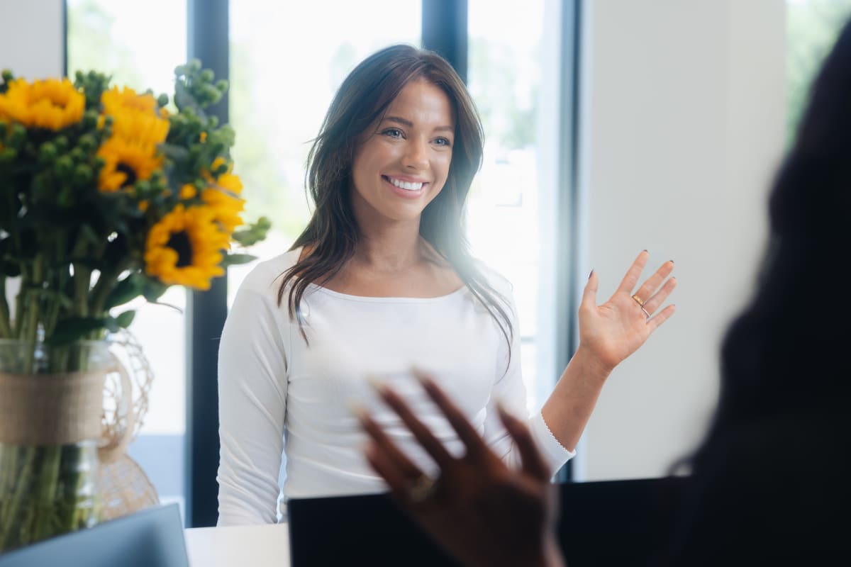 Woman smiling brightly at camera with natural, confident expression by bright window