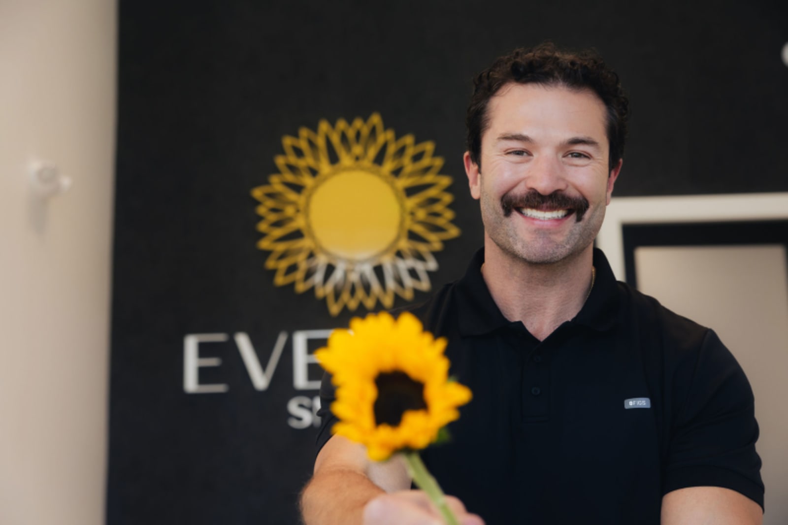 Male dentist holding sunflower at Evelina Smiles practice, smiling at camera