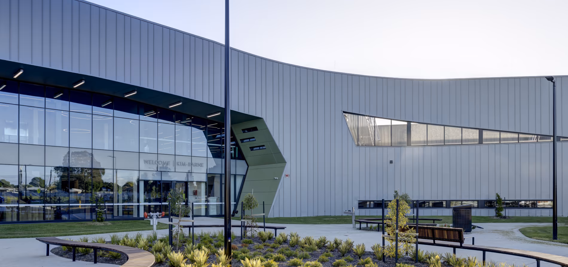 Modern building with large glass windows, geometric design, and landscaped outdoor seating area with curved wooden benches.
