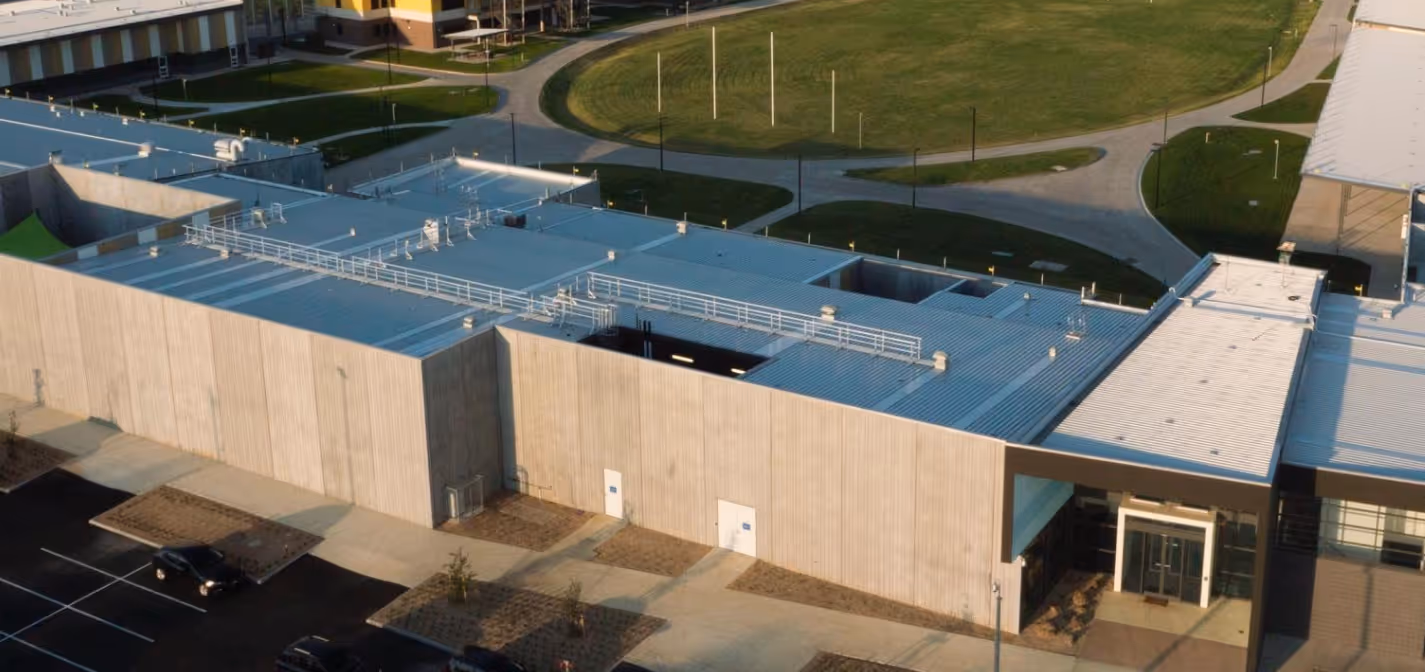 Aerial view of a modern building with a flat roof, concrete walls, and a parking lot with a few cars parked.