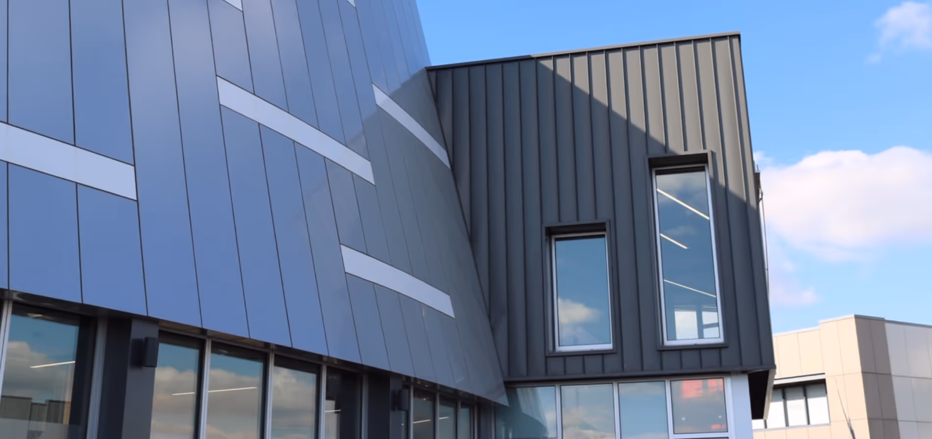 Modern building facade with blue reflective glass panels and dark vertical siding under a bright sky.