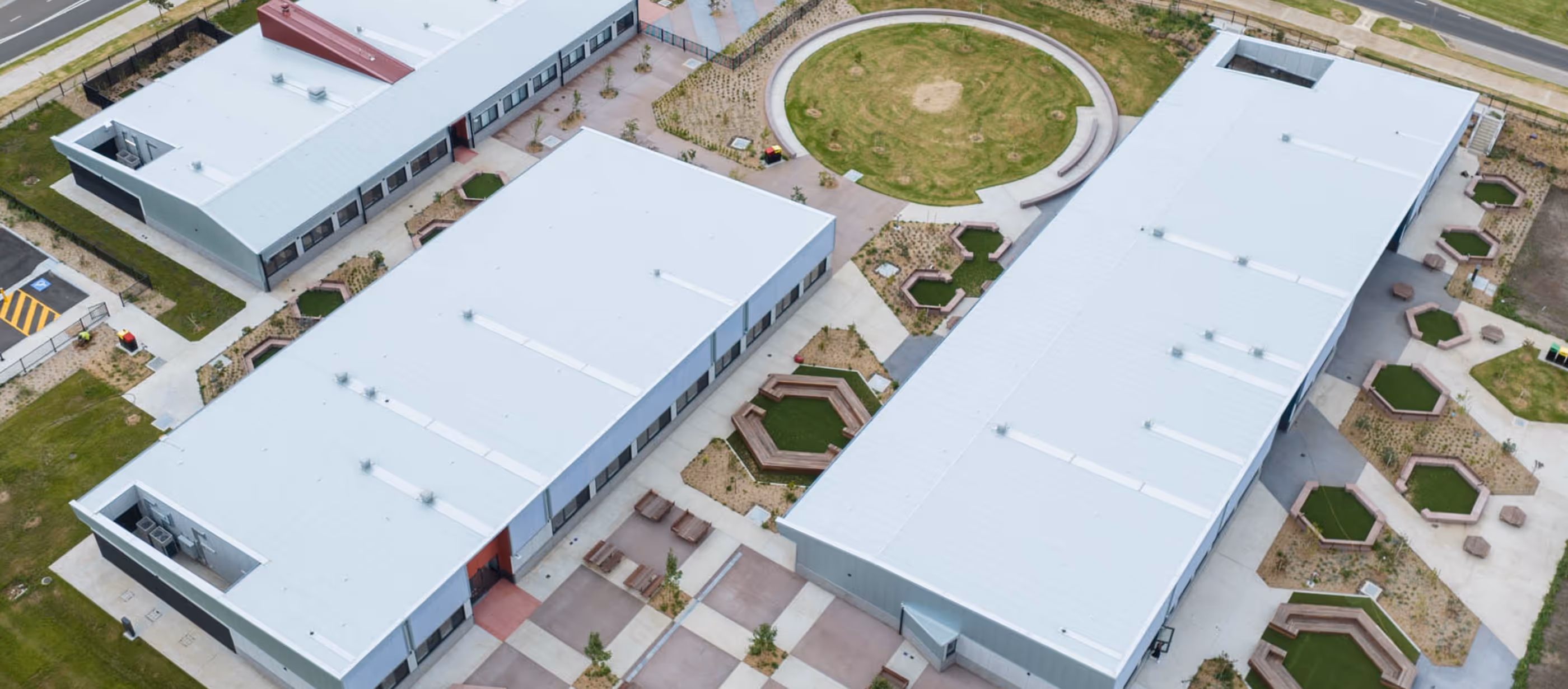 Aerial view of a modern school campus with multiple white-roofed buildings and hexagonal outdoor seating areas.