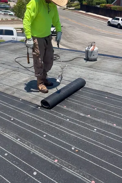 Worker installing torch down roofing with modified bitumen membrane on flat roof in Carson CA