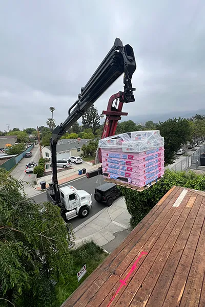 Knuckle boom truck delivering roofing materials for 3B Roofing in Paramount California, lifting pallets of shingles to a rooftop using an articulated crane for safe roof delivery