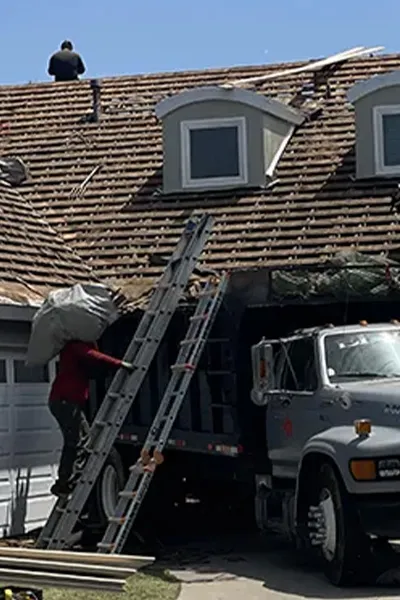 Roofing crew repairing and replacing a residential roof in Lennox CA, removing old shingles and loading debris into a truck while 3B Roofing contractors safely work on roof structure in Los Angeles County