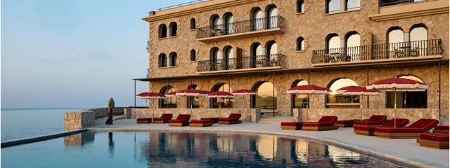 Stone facade and seafront pool lined with red loungers at Zannier Île de Bendor