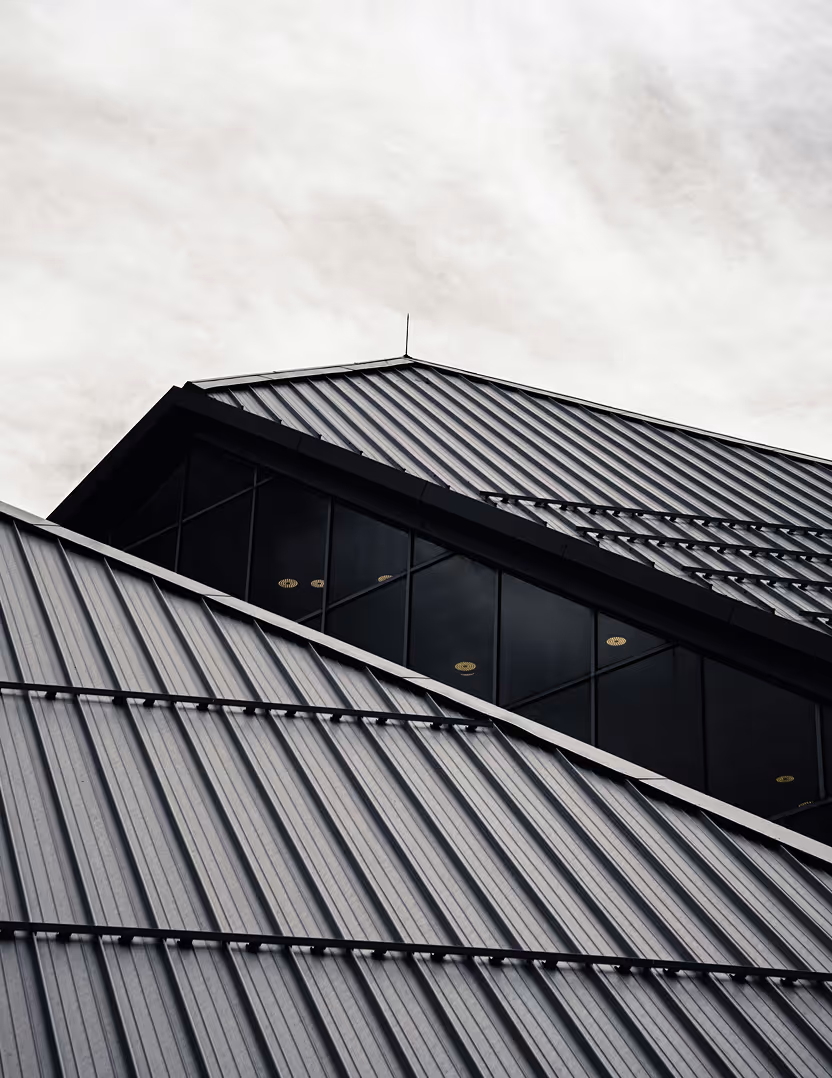 Close-up of a modern building roof with sleek metal panels and a narrow window section reflecting ceiling lights.