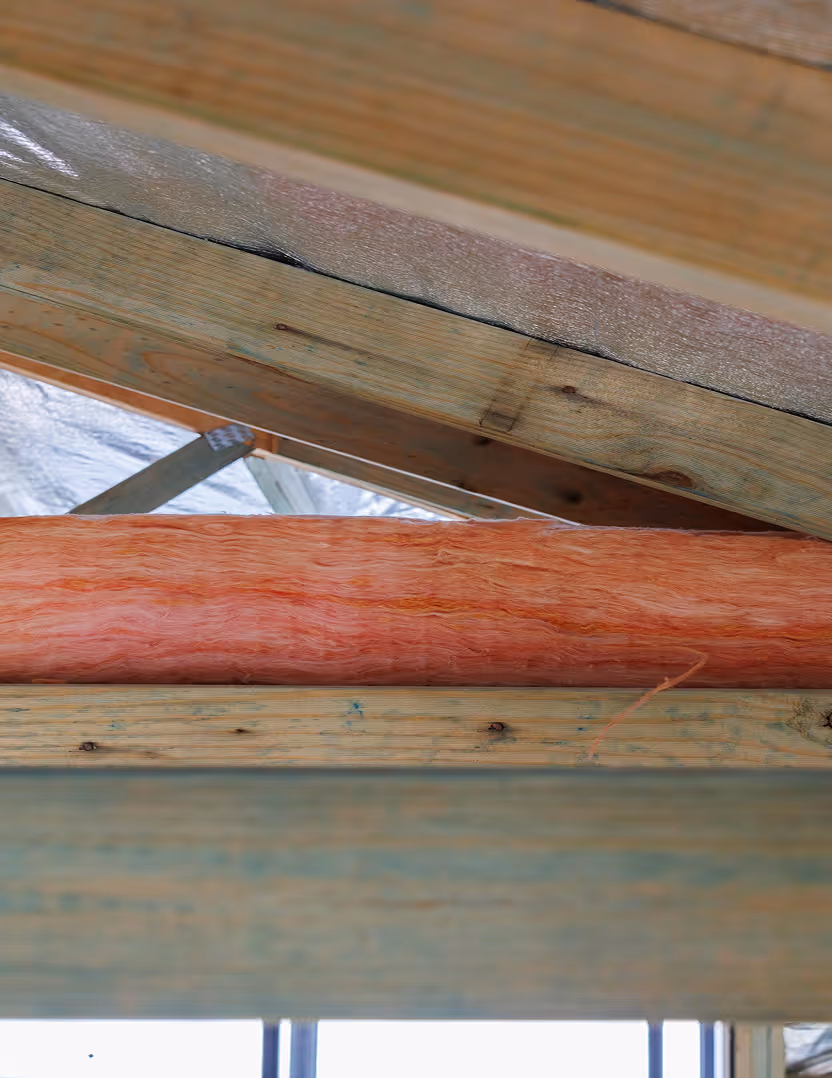 Close-up view of wooden beams and pink fiberglass insulation installed between them in a building under construction.