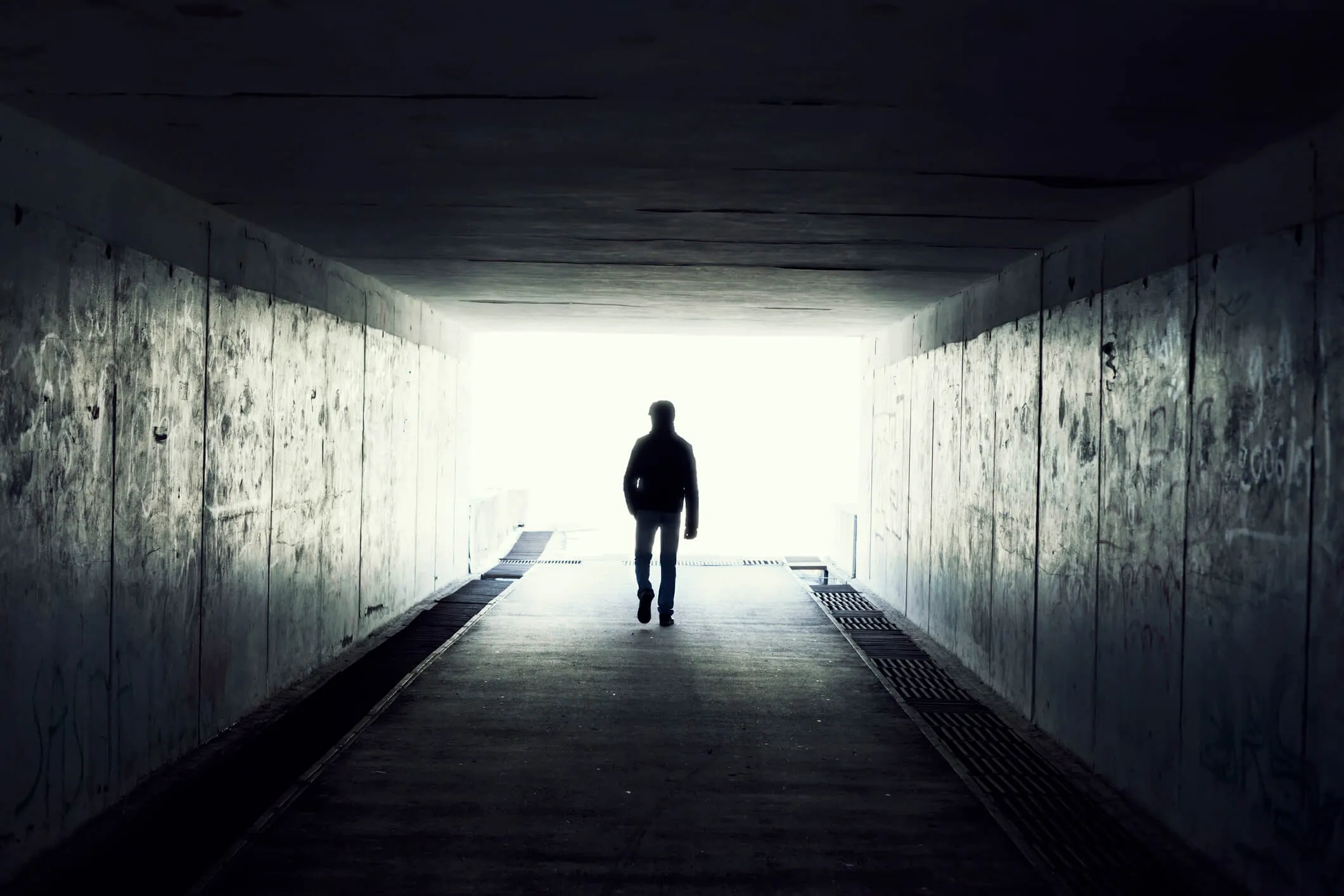 Silhouette of a man walking out of a dark tunnel toward the light