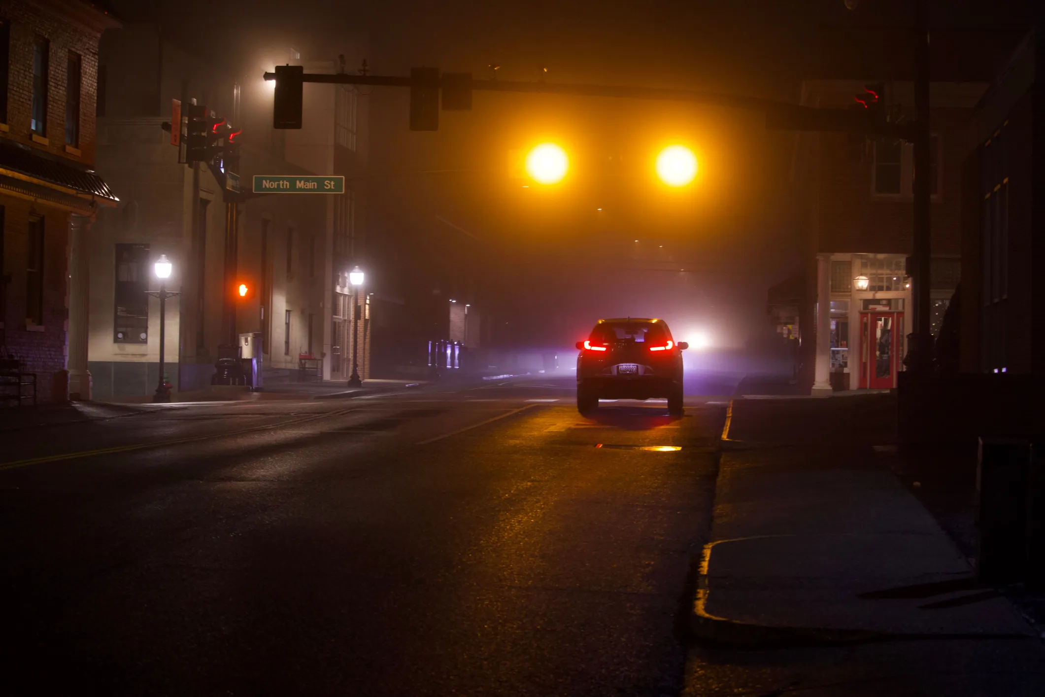 Car stopped at a traffic light on a foggy downtown street at night