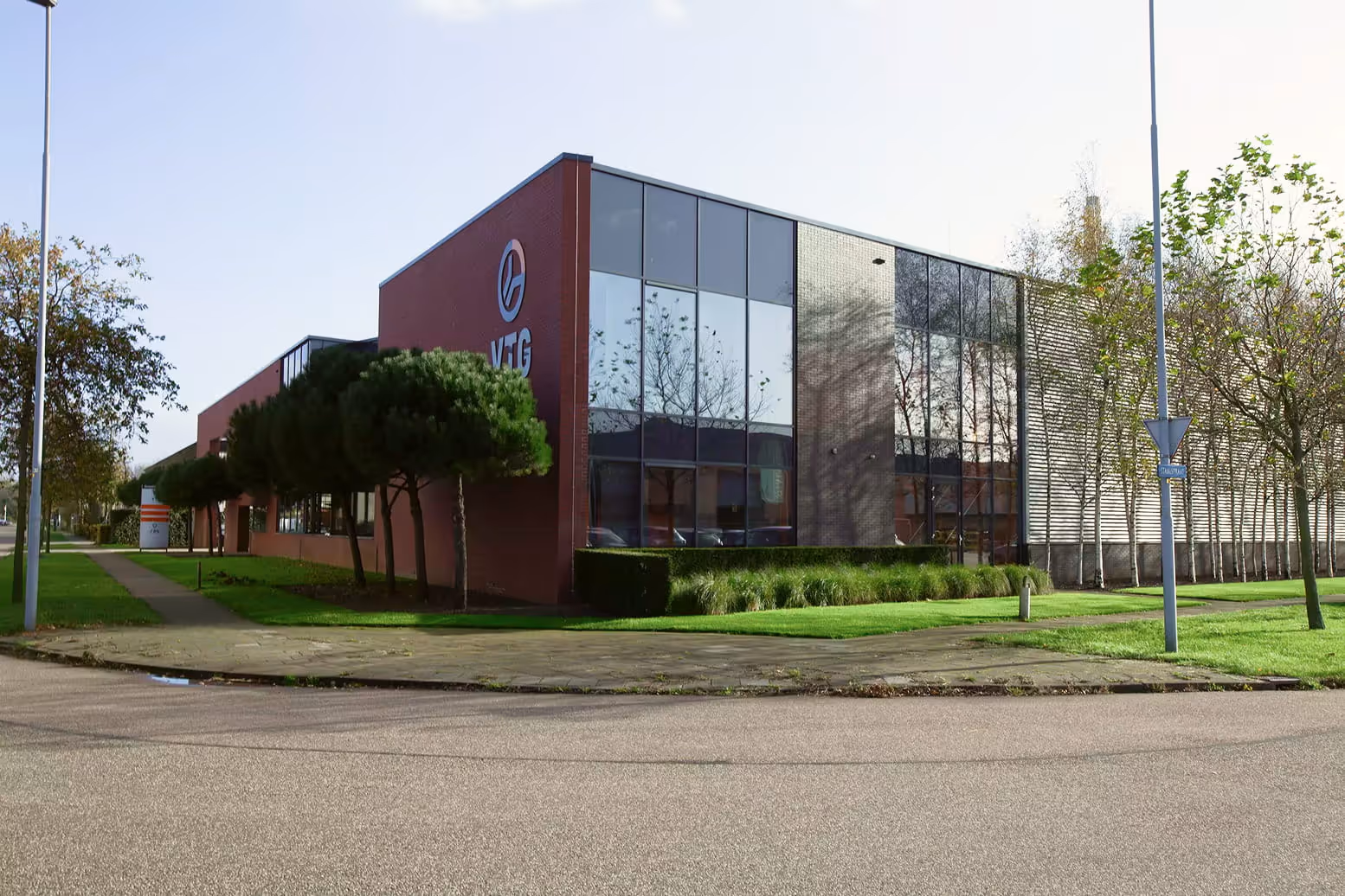 Moderne bedrijfsgebouwen met grote ramen, bomen en groen langs een rustige straat.