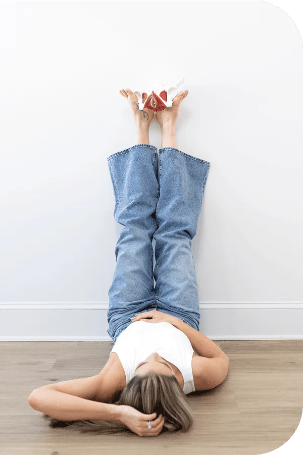 Dr. Lynne DiPirro lying with her legs up the wall, balancing a pelvis model on her feet