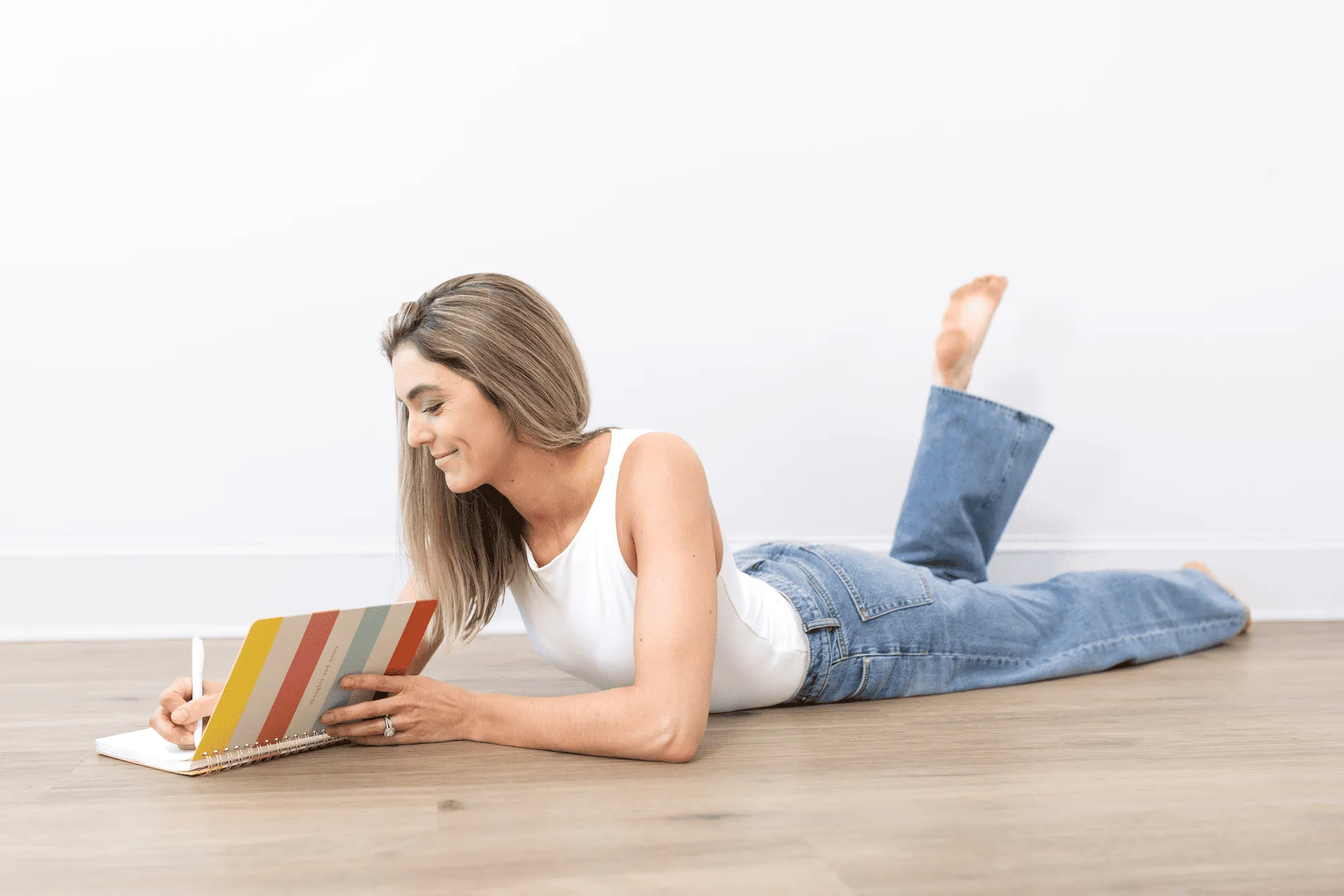 Dr. Lynne DiPirro lying on the floor writing in a striped notebook, pelvic health education made simple