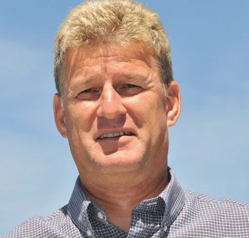 Mann mit hellem Haar trägt kariertes Hemd und steht bei blauem Himmel.