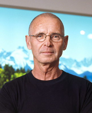 Porträt einer Person mit Brille und schwarzem T-Shirt vor einem Bild von Bergen.