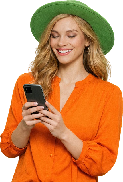 Sieviete zaļā cepurē un oranžā krekliņā smaida, skatoties uz mobilo tālruni.