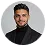 Smiling man with dark hair and beard wearing a black sweater against a white background.