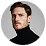 Man with short brown hair and light skin wearing a black turtleneck against a white background.