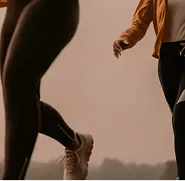 Two people jogging outdoors wearing athletic leggings and sneakers during a cloudy day.