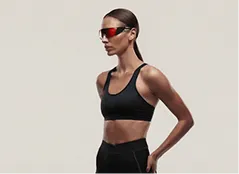 Fit woman in black sportswear and red sunglasses standing in profile with hands on hips.
