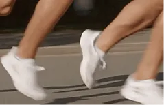 Close-up of two people running wearing white athletic shoes on a paved surface.