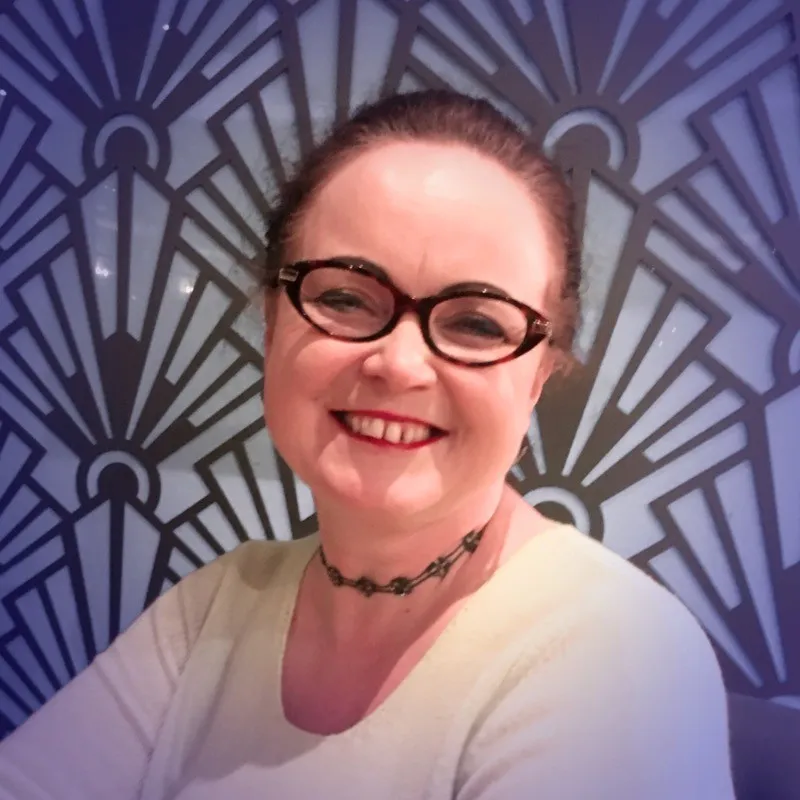 Smiling woman with glasses and choker necklace against a patterned blue and black wall.