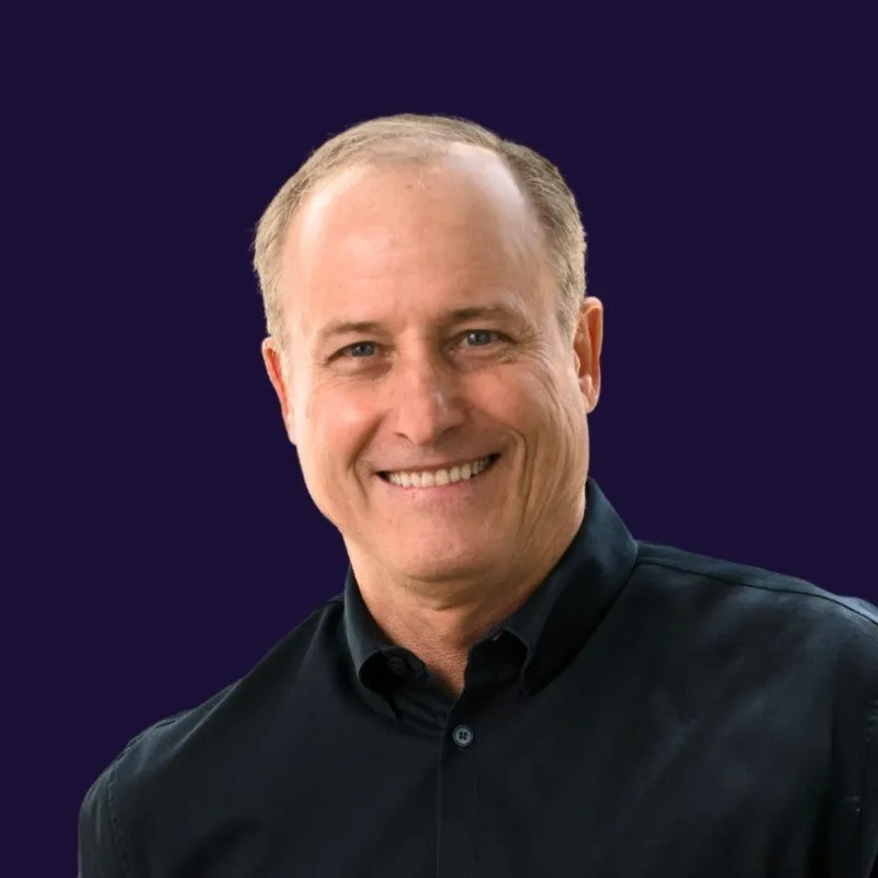 Smiling middle-aged man with short hair wearing a black button-up shirt on a dark purple background.