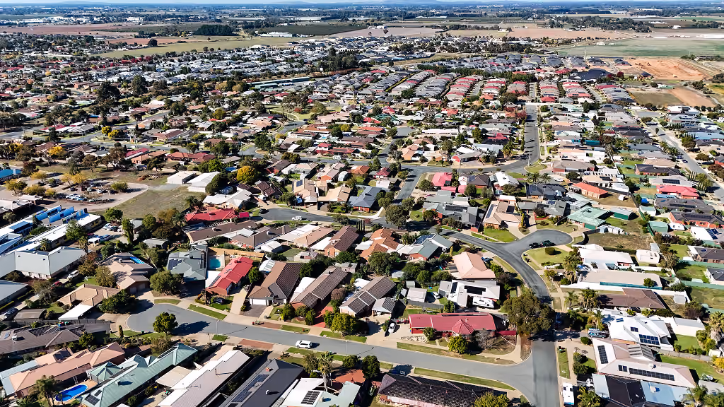 Aerial view of a residential neighborhood with houses, roads, and scattered trees under clear skies.