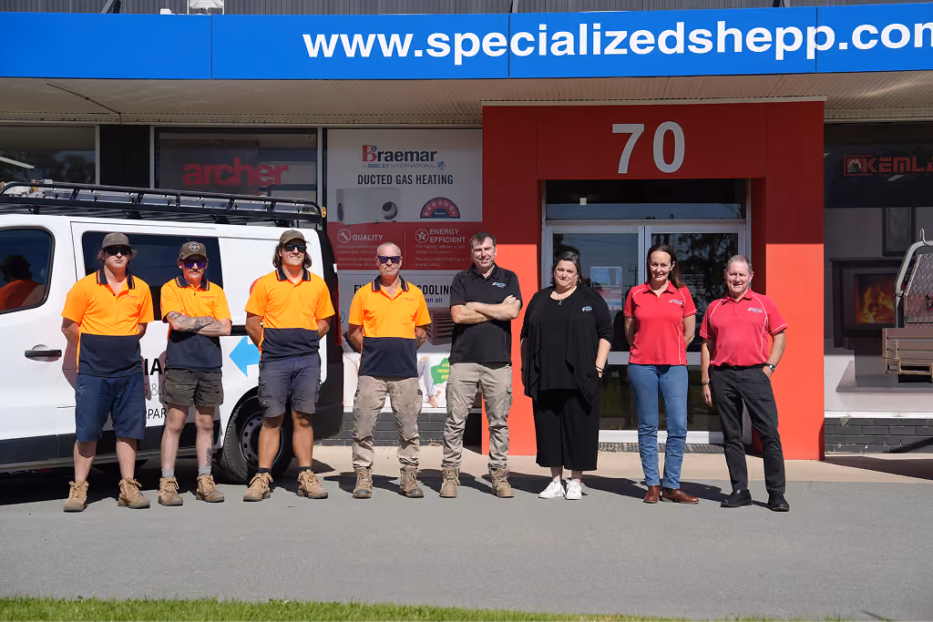 Eight people standing in a row outside a business with a blue sign and red door numbered 70.