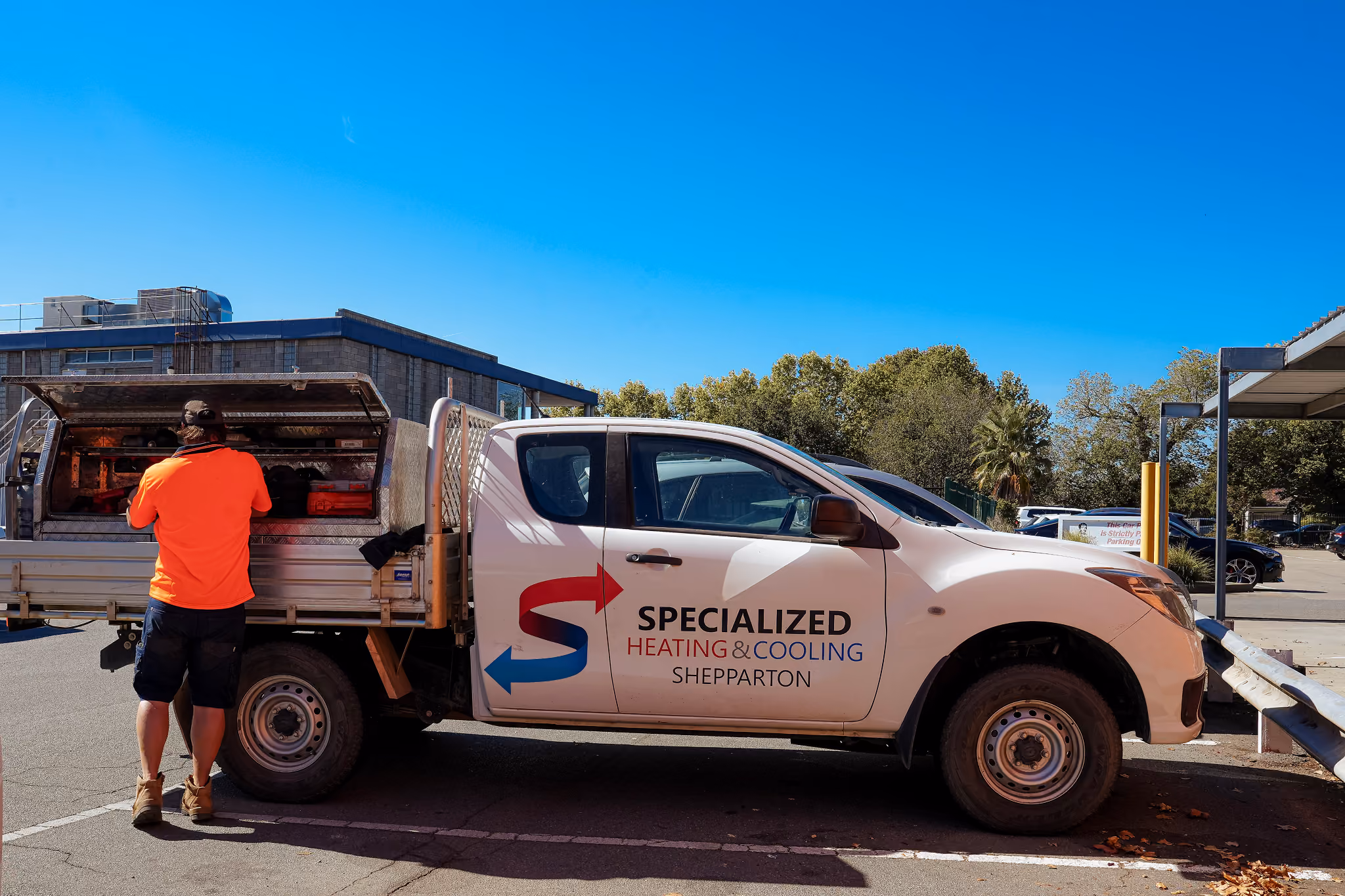 Worker in orange shirt accessing tools in back of a white Specialized Heating & Cooling Shepparton truck.