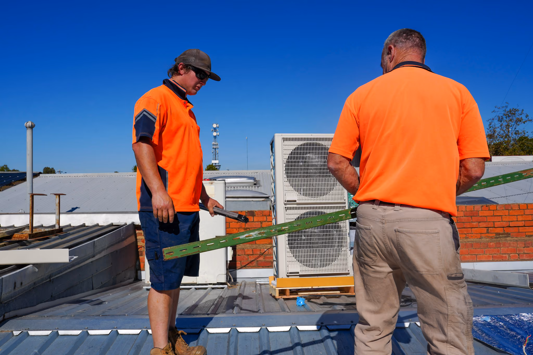 Two men working on a metal roof installation on a sunny day with a blue sky.