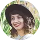 Woman with curly hair wearing a black wide-brim hat and a bright smile outdoors.